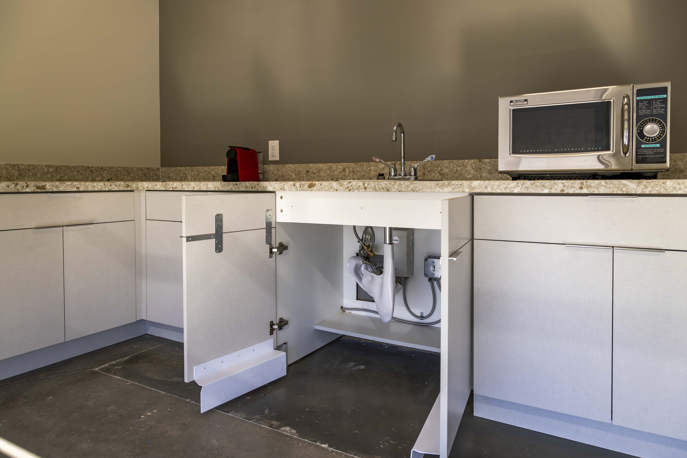 Open breakroom cabinet showing under-sink plumbing and tankless water heater installation.