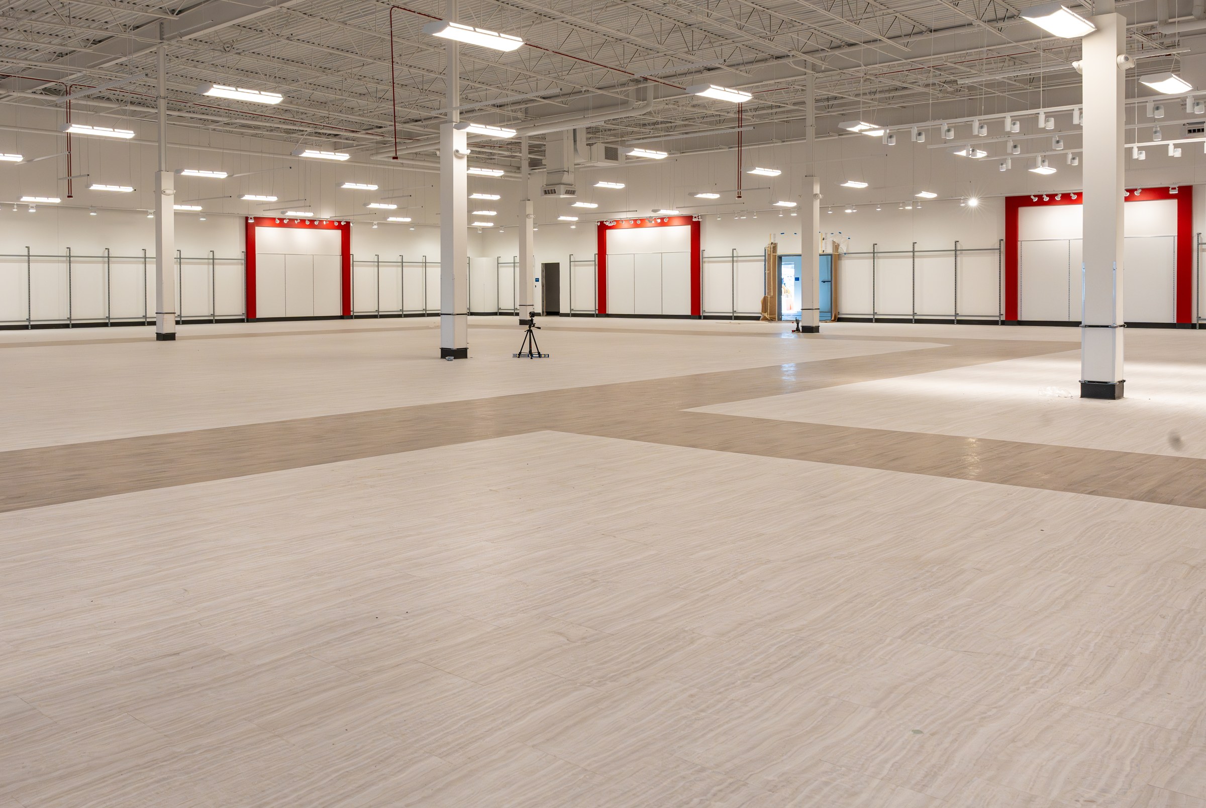 Wide sales floor shot showing the two-tone wood-look flooring transition and a camera tripod.