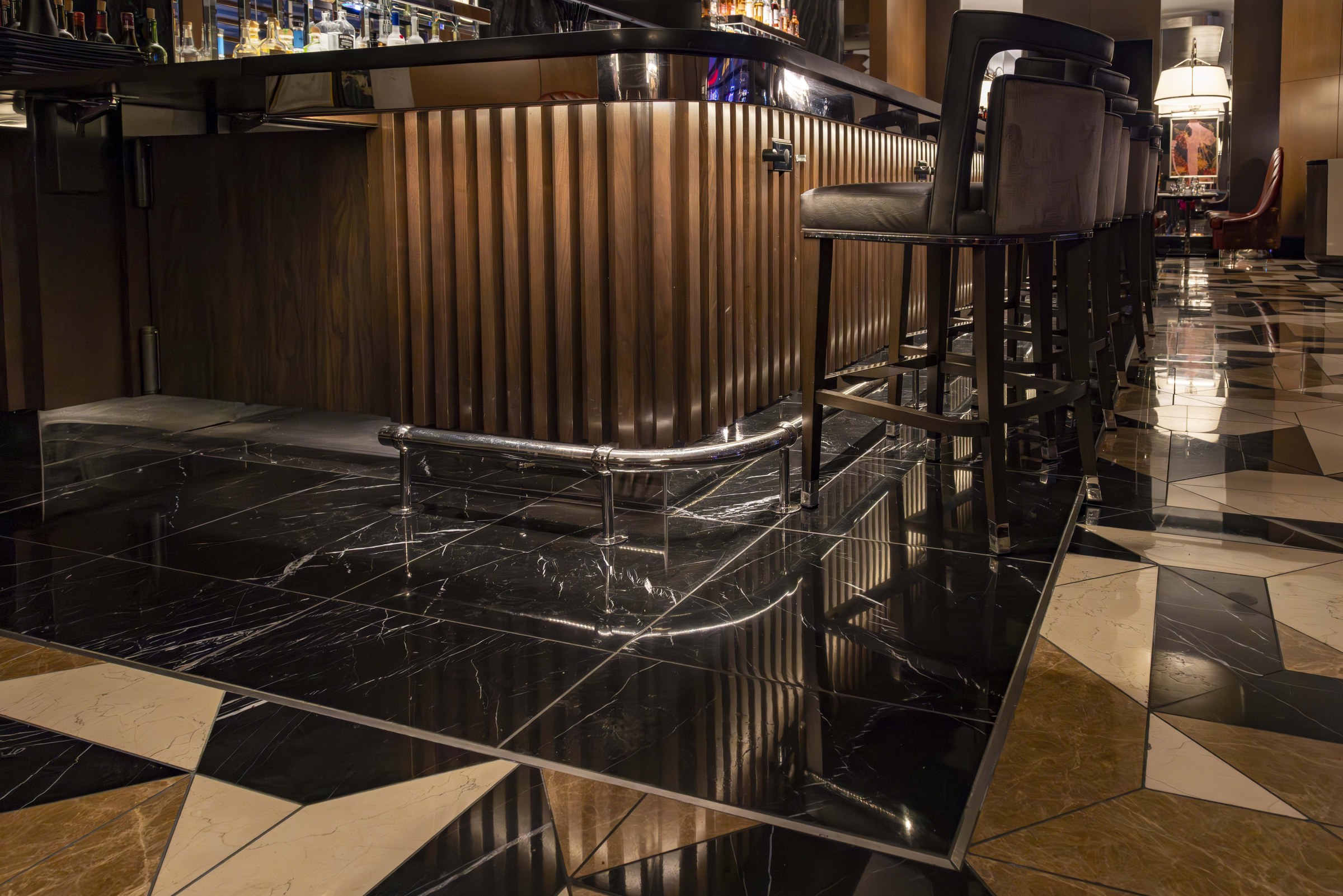 Bar stools over the geometric marble tile floor with black marble bar front at William B's Steakhouse.